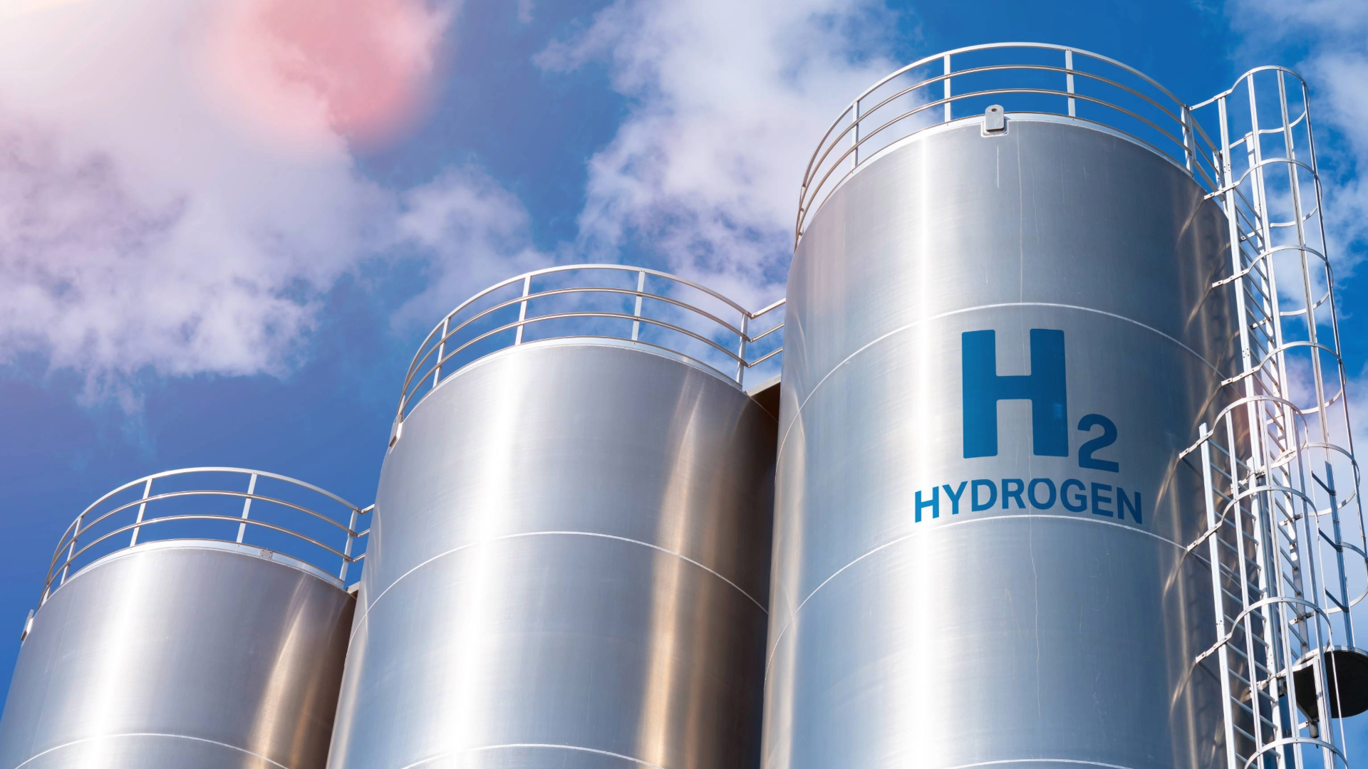 Several large metallic tanks labeled 'H2' and 'HYDROGEN' against a clear blue sky, with some clouds visible.