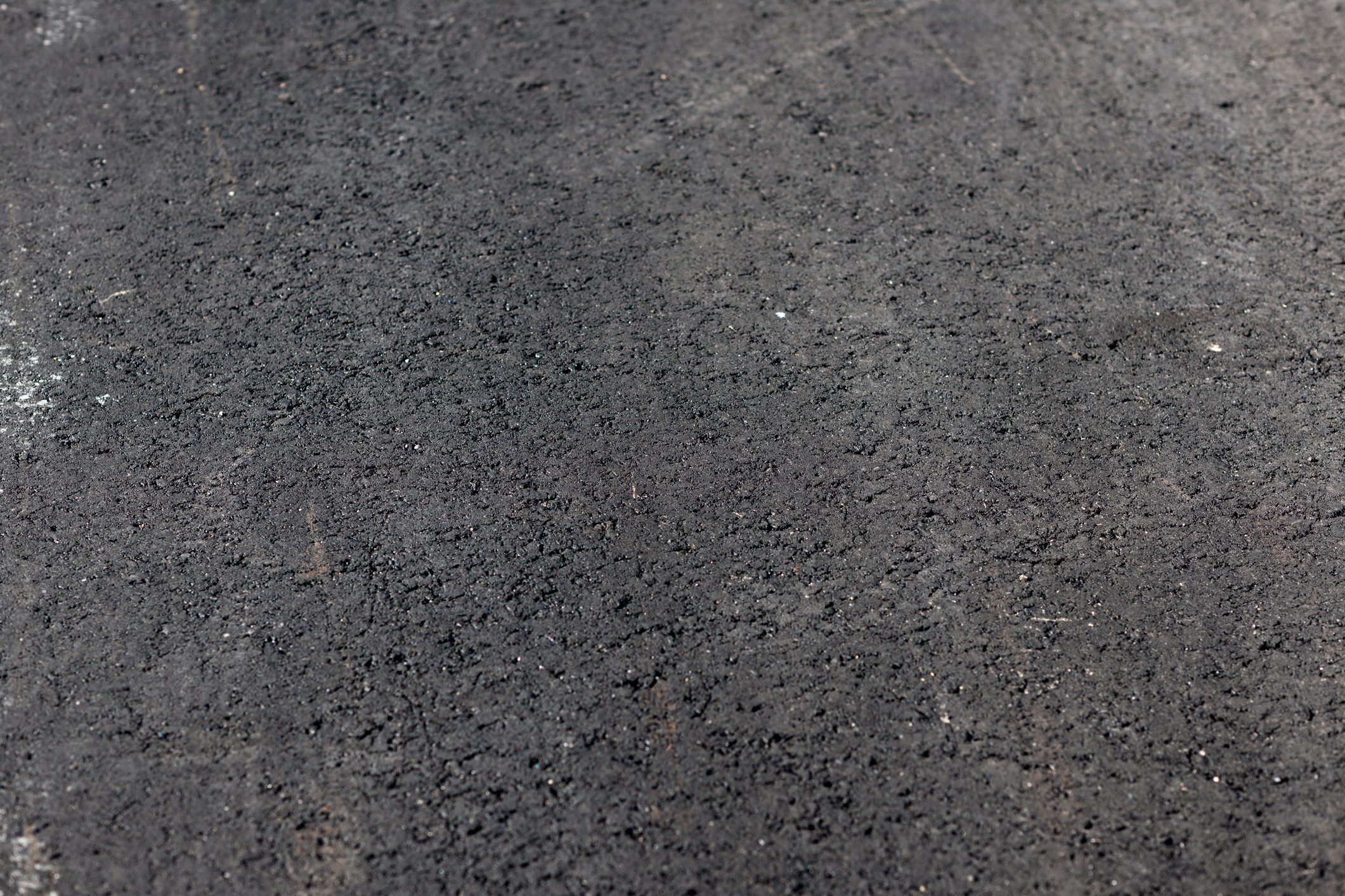 Close-up view of a textured black asphalt surface, showing small pebbles and a rough finish.