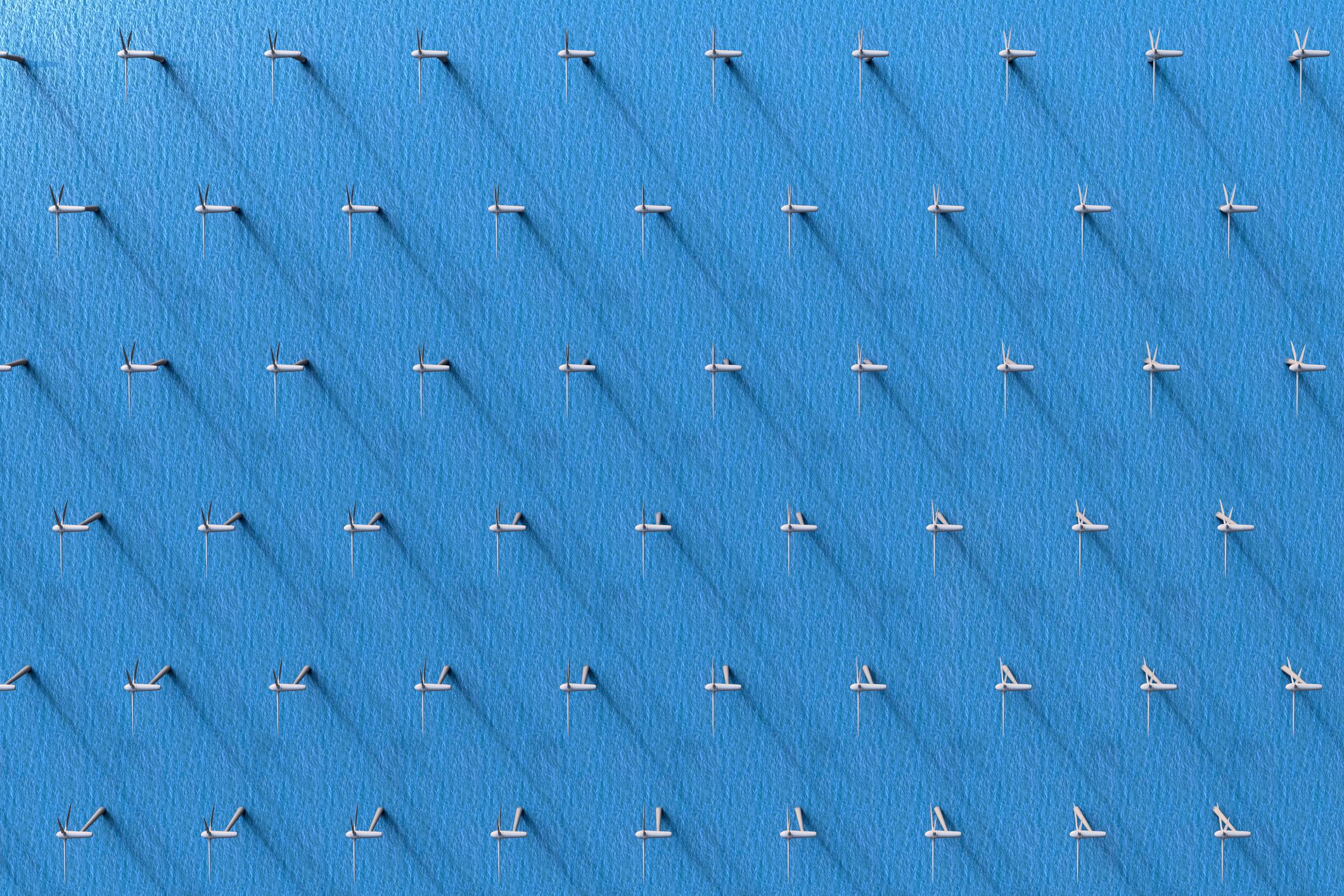 An aerial view of a large grid of white wind turbines set against a blue background, casting long shadows on the surface.