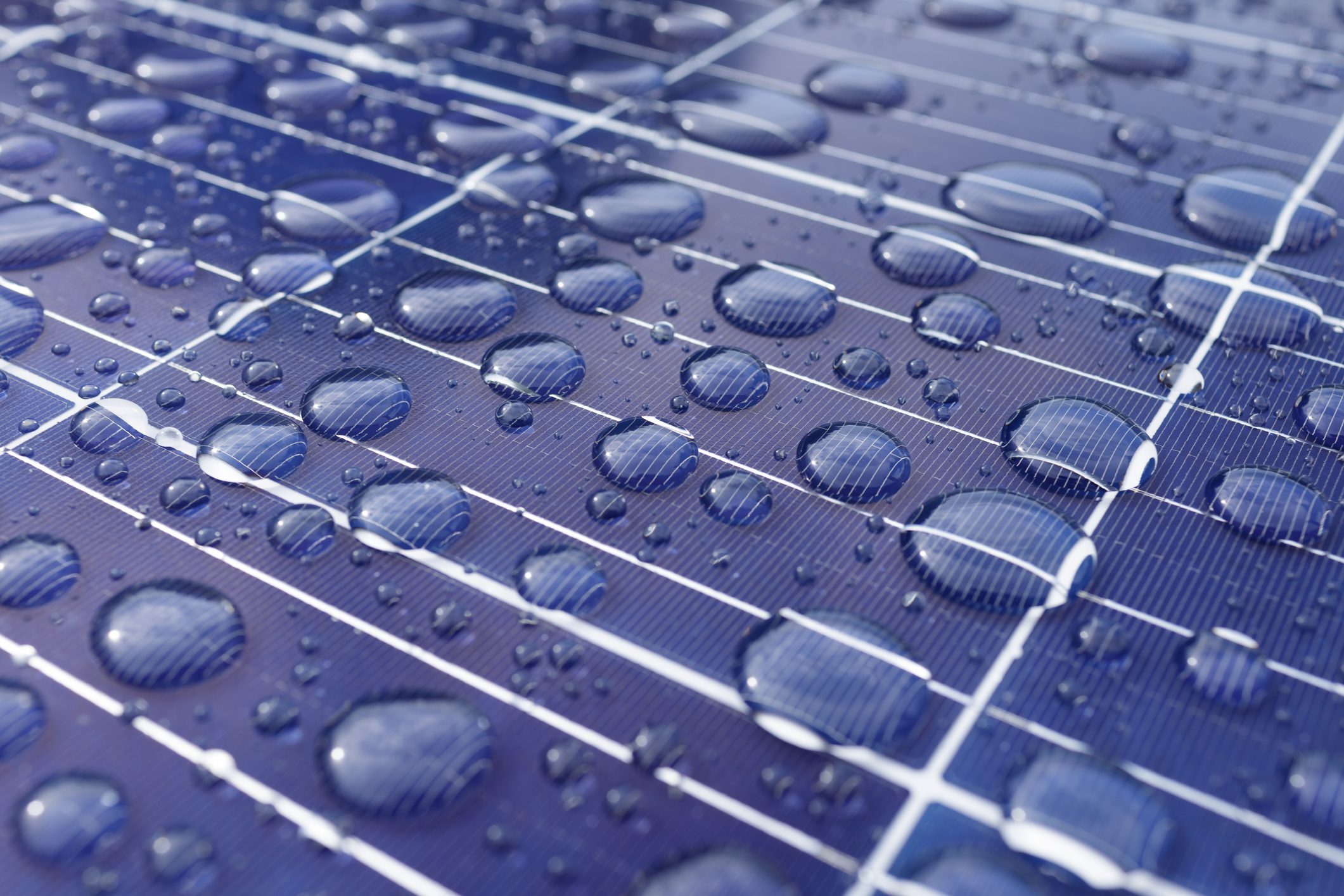 Close-up of a solar panel surface covered with water droplets, highlighting the texture and reflections on the dark blue cells.