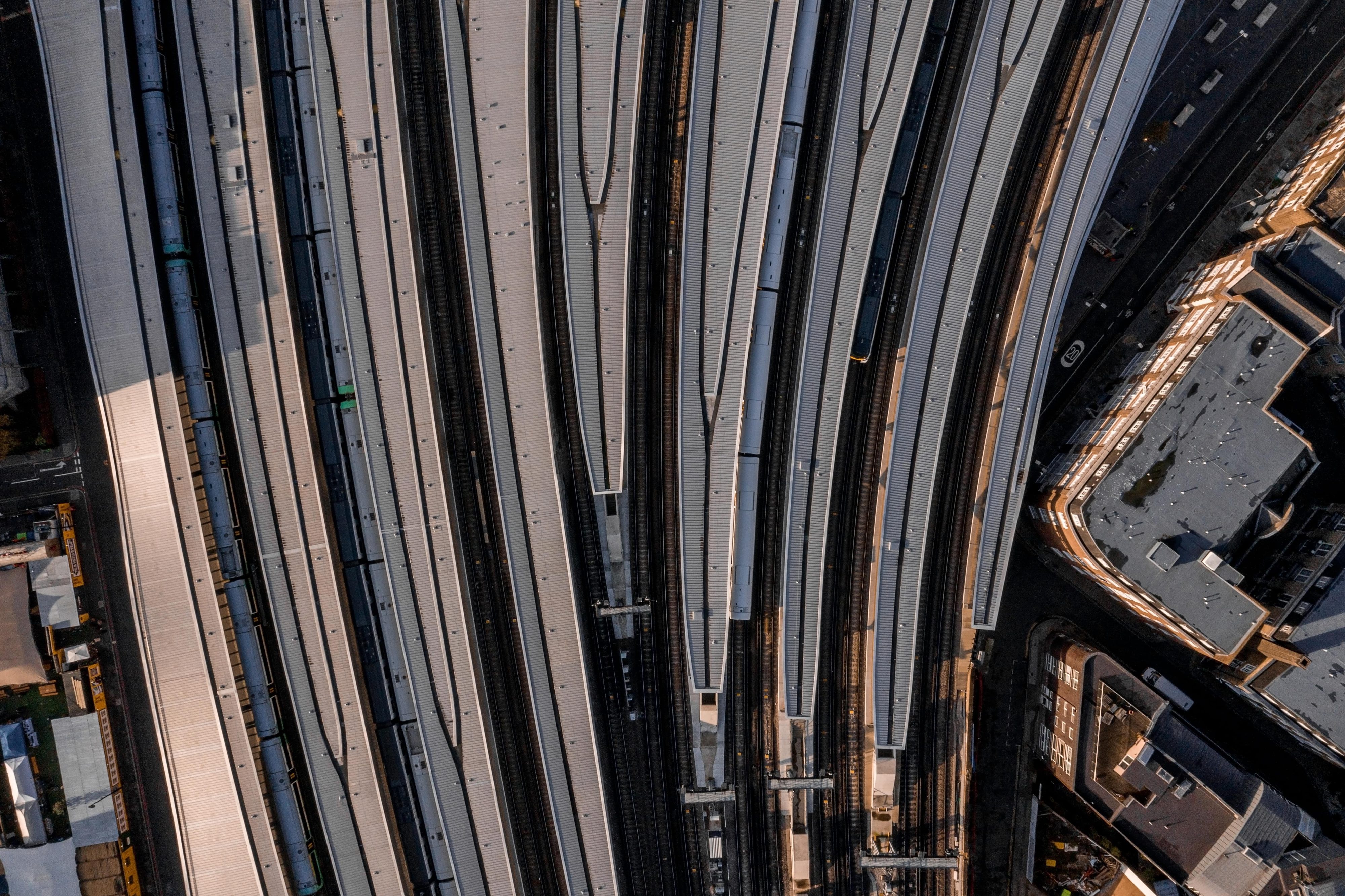 An aerial view of railway tracks curving through a city, with buildings and rooftops visible in the surrounding area. The tracks are arranged in parallel lines, some covered with awnings.