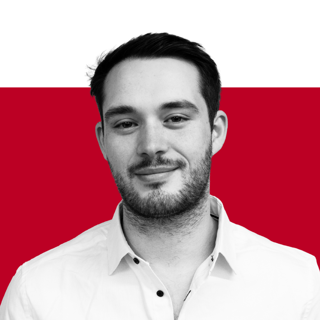 A man with short dark hair and a beard smiling, wearing a white button-up shirt, with a black and red background.