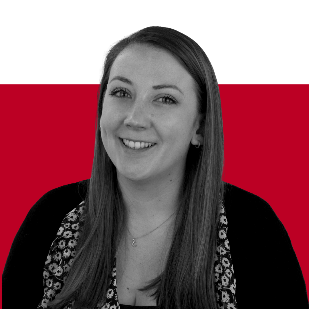 A woman smiling at the camera, with long brown hair, wearing a black cardigan over a white floral top, against a background of solid red and black colors.