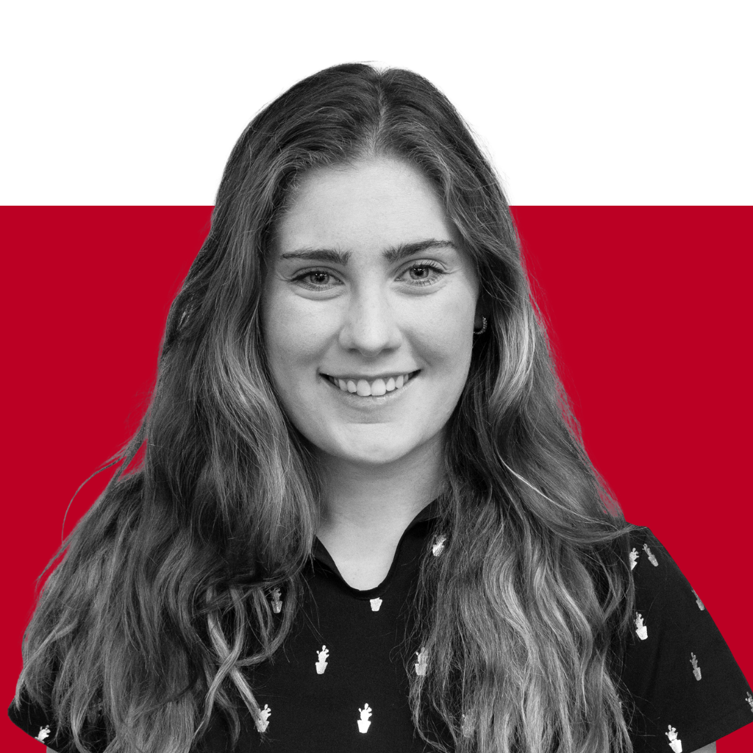 A smiling person with long wavy hair, wearing a black shirt with small white patterns, is photographed against a red and black background.