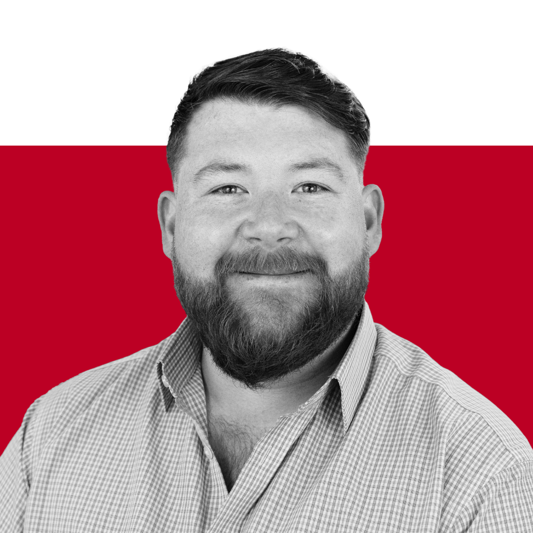 A man with a beard wearing a checkered shirt, smiling at the camera. The background features solid colors, predominantly red and black.