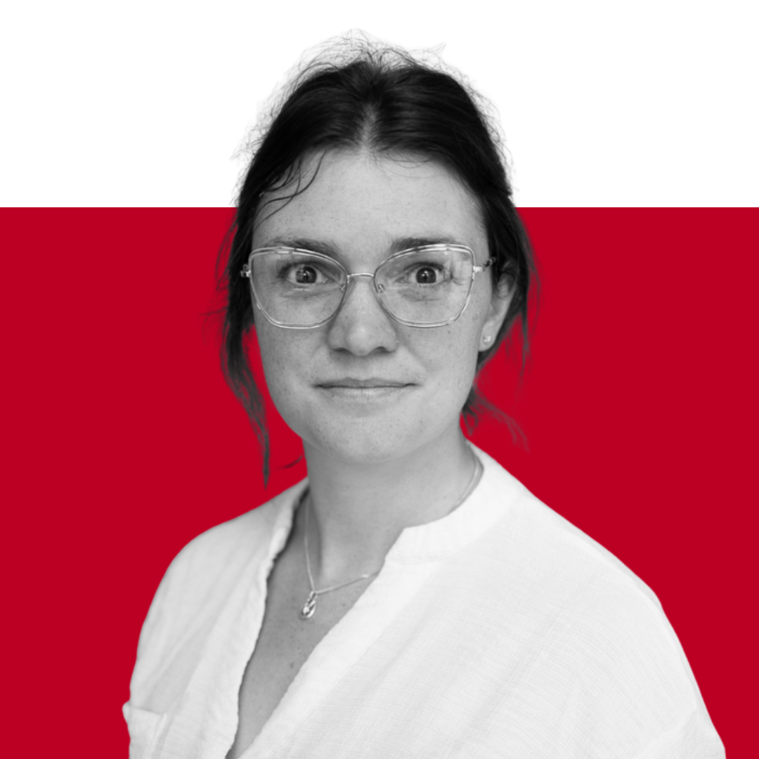 A woman with glasses and dark hair is positioned against a red background, looking directly at the camera. She wears a white blouse and has an attentive expression.