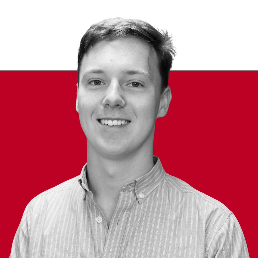 A young man smiling, wearing a button-up shirt, in front of a simple red and black background.