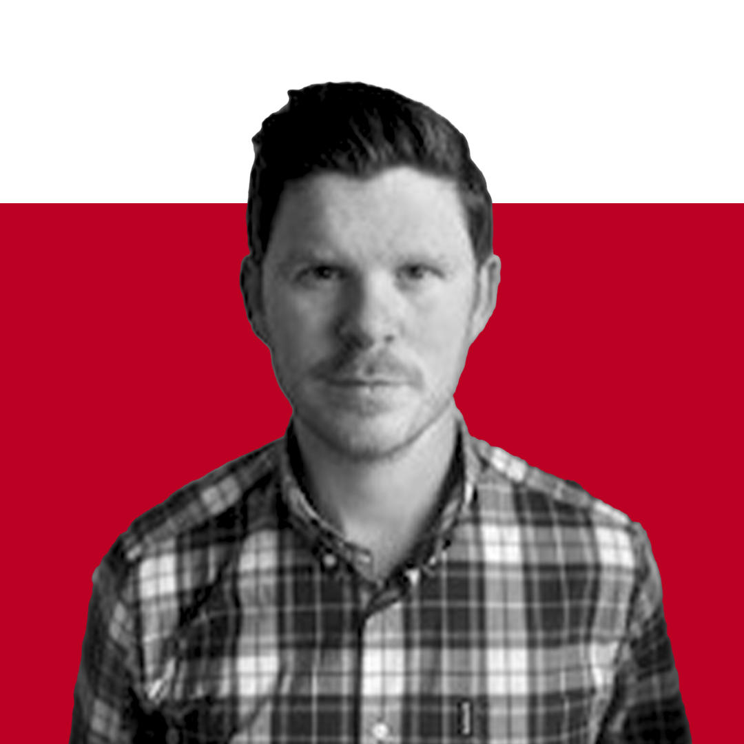 A man with short hair and a serious expression wearing a checkered shirt, set against a background of solid black and red colors.
