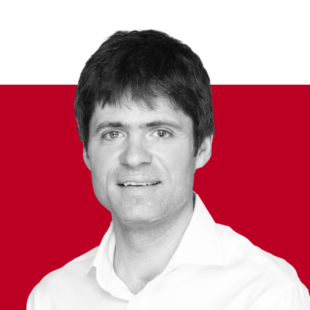 A headshot of a man with short dark hair wearing a white shirt. The background features a gradient of black and red.