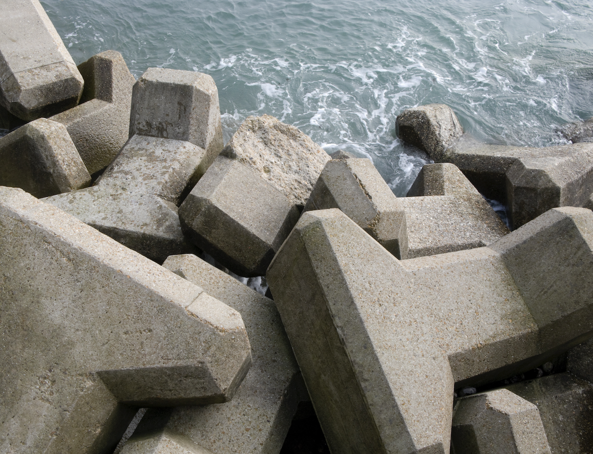 Concrete tetrapods arranged on the shore, partially submerged in water with waves gently lapping against them.