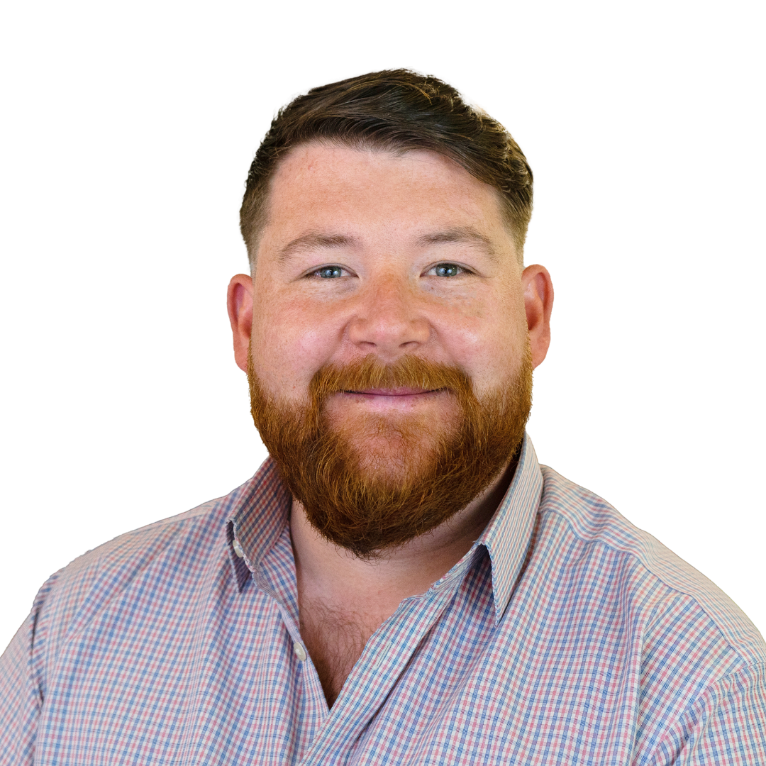 A man with a beard, wearing a plaid button-up shirt, smiles at the camera. The background is plain, emphasizing his facial features and expression.