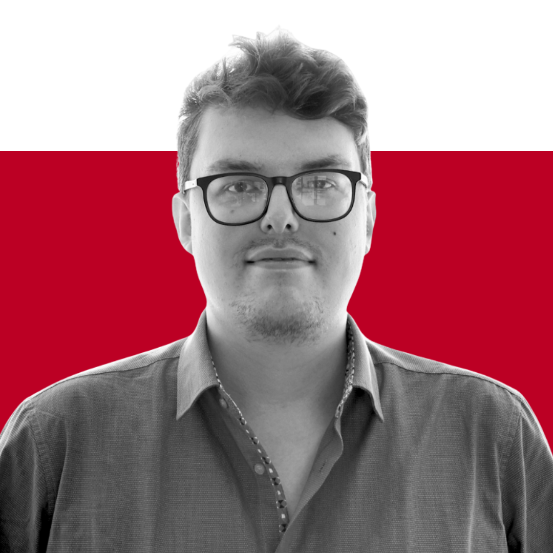 A man with glasses wearing a button-up shirt, standing against a background with a gradient of red and black colors.