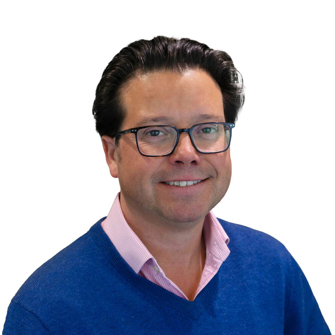 A man wearing glasses and a blue sweater over a pink collared shirt, smiling against a white background.