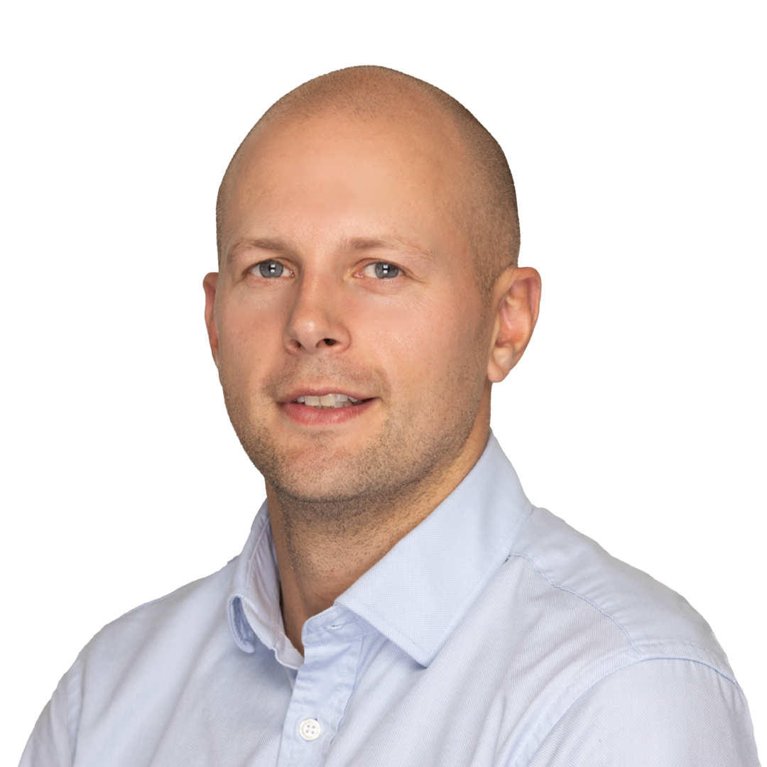 A professional portrait of a man with a shaved head wearing a light blue button-down shirt, smiling against a white background.