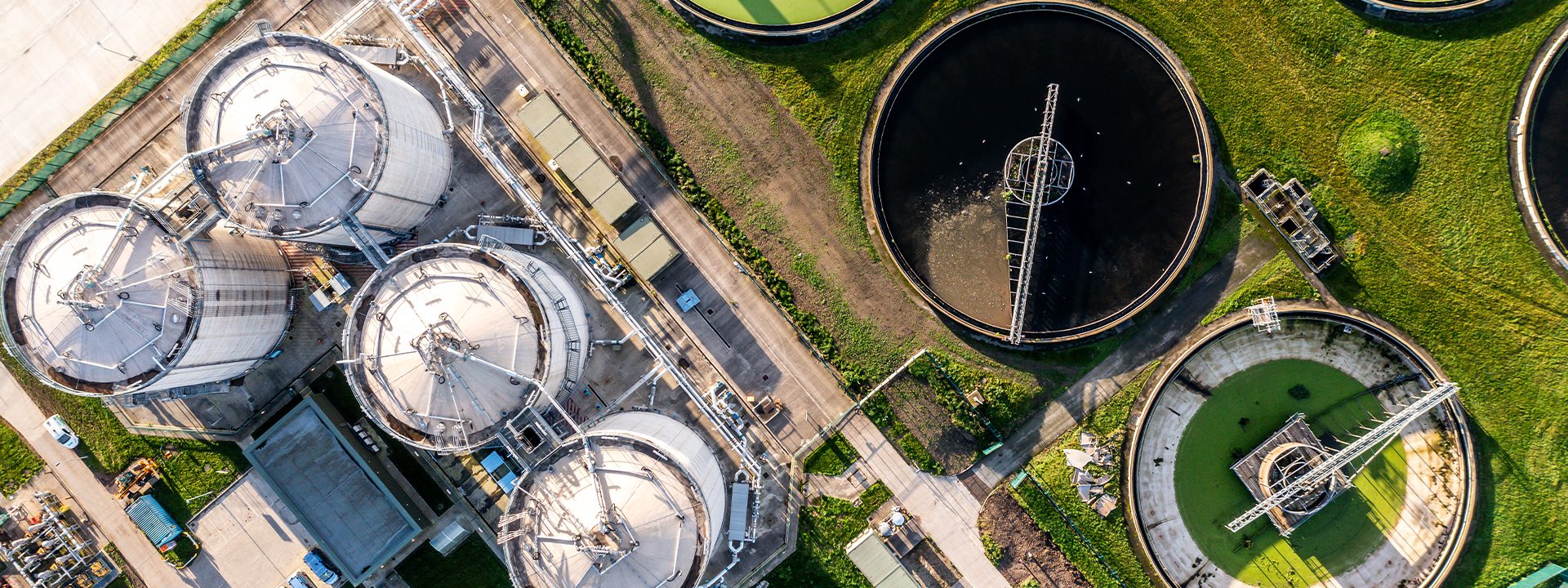 An aerial view of industrial storage tanks and processing facilities, featuring circular tanks with varying contents and green grass surrounding the area.
